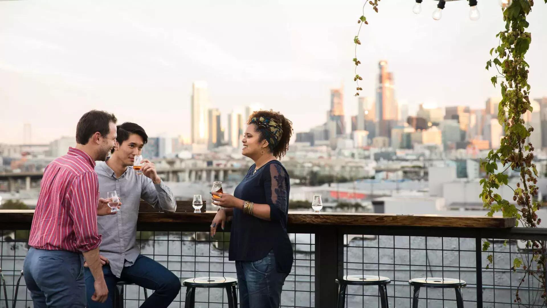 Tre persone si riuniscono attorno a un tavolo all'aperto sulla terrazza sul tetto della Anchor Distilling a San Francisco, California.