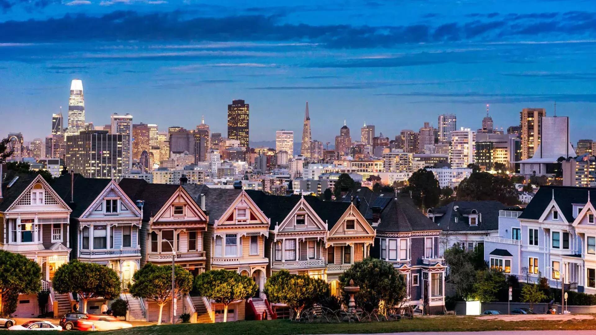 夕暮れのサンフランシスコのスカイラインを背景に、有名なアラモ・スクエアのペインテッド・レディが描かれています。