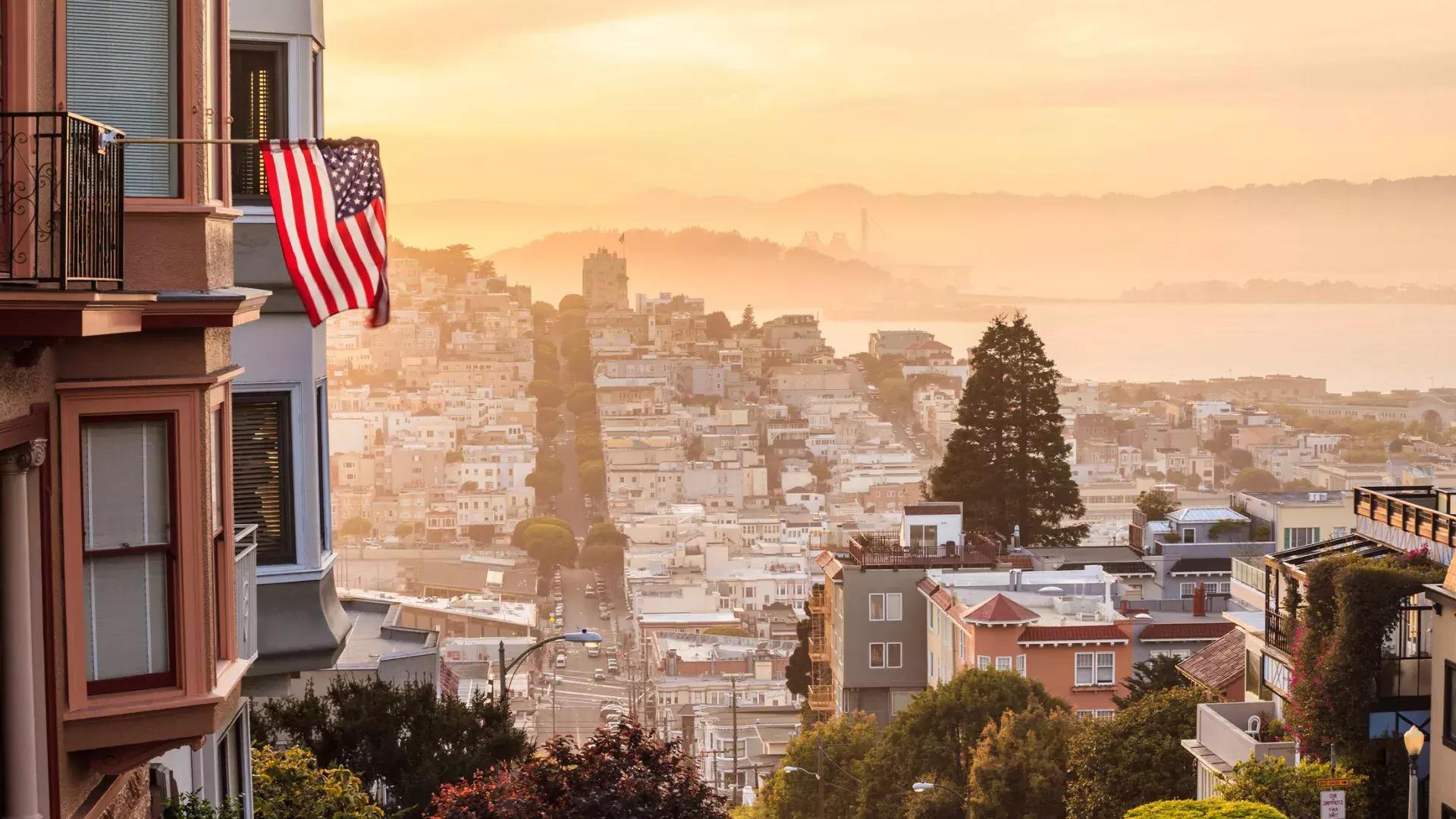 Uma vista de São Francisco do topo de uma colina, com uma bandeira americana tremulando em primeiro plano.