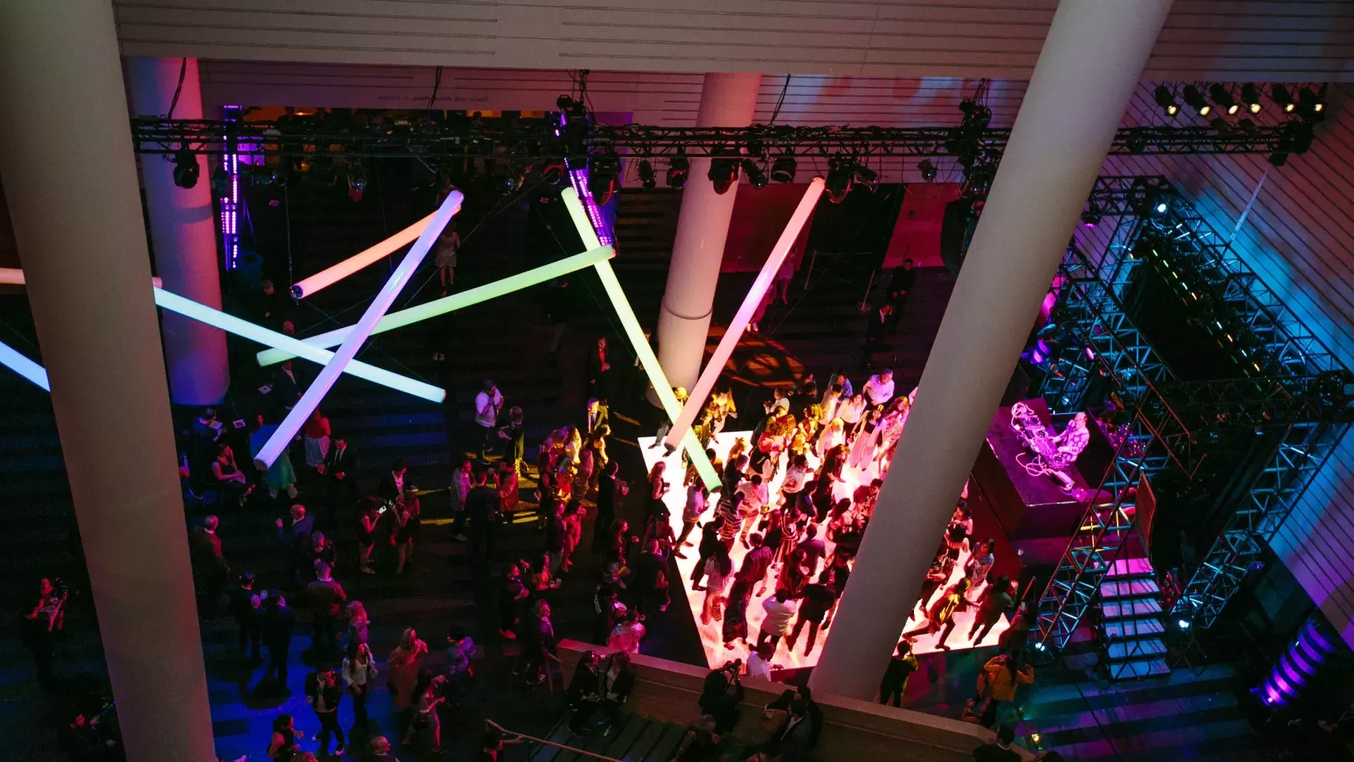 Image of people on a dance floor lit by rainbow neon lights hanging from ceiling