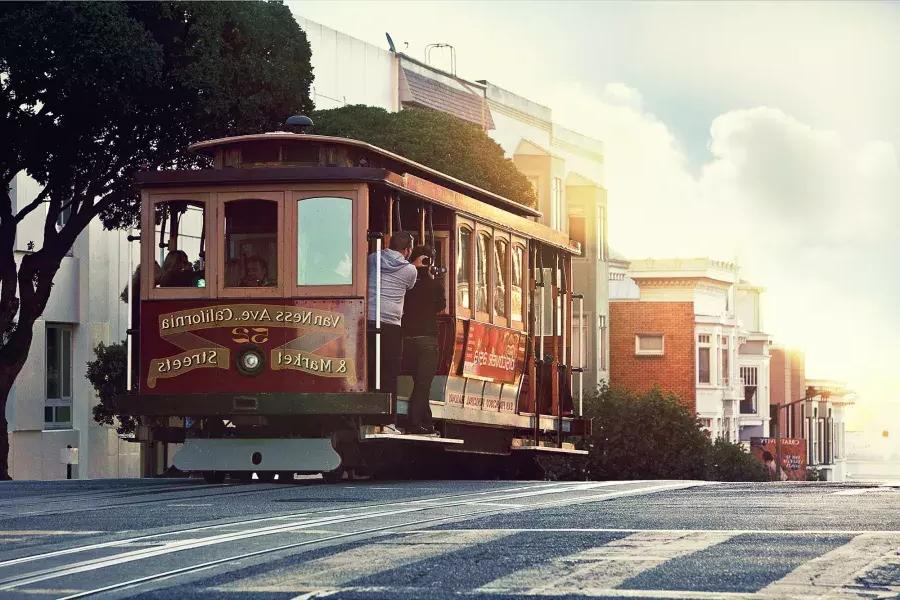Un teleférico rodea una colina en San Francisco con pasajeros mirando por la ventana.