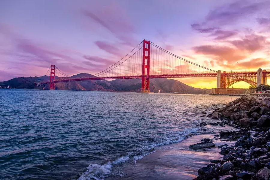 夕暮れ時のゴールデン ゲート ブリッジと色とりどりの空、前景にサンフランシスコ湾。