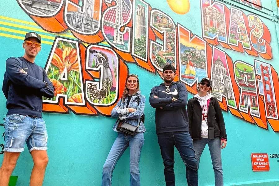 Trendy visitors pose in front of a San Francisco mural.