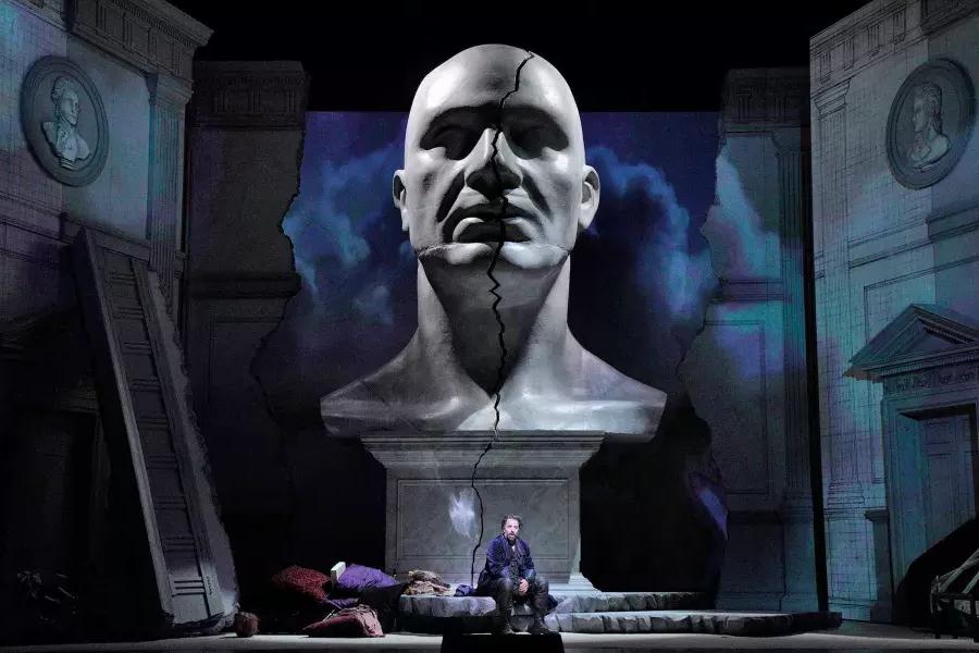 Un buste géant représentant un homme domine deux acteurs sur scène dans une production de Don Giovanni 在贝博体彩app.