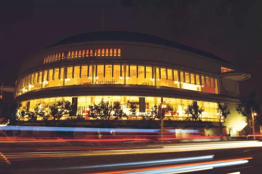 Außenansicht der Louise M. 戴维斯交响音乐厅在晚上有灯光闪烁的车辆通过。.