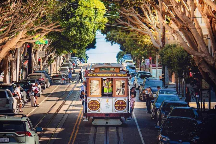 나무가 늘어선 거리에 샌프란시스코 케이블카가 다가옵니다.