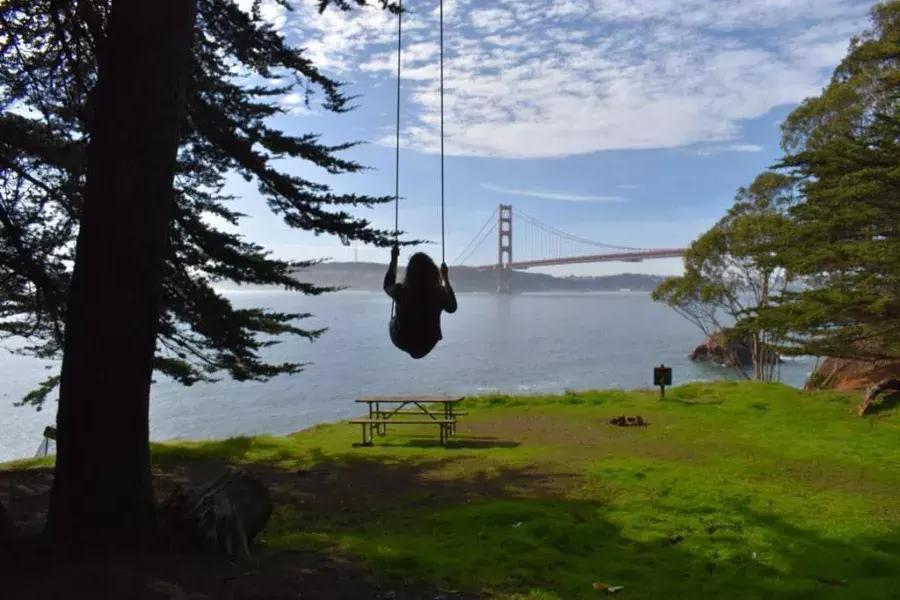 一个女人在秋千树俯瞰金门大桥. San Francisco, California.