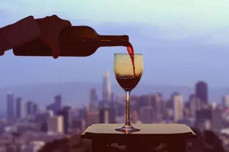 A glass of red wine being poured with the San Francisco skyline visible out the window.