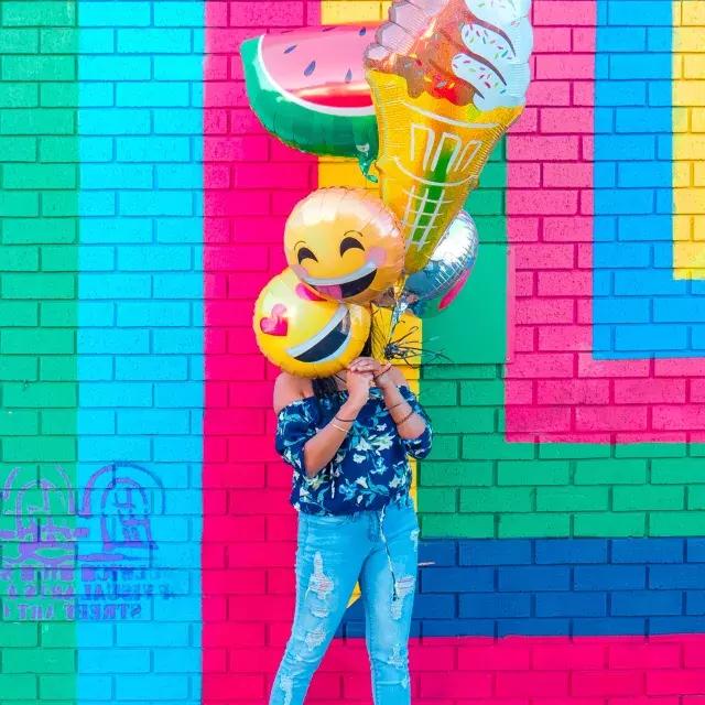 Ein Mädchen feiert ihren Geburtstag mit Luftballons vor einem bunten Wandgemälde.