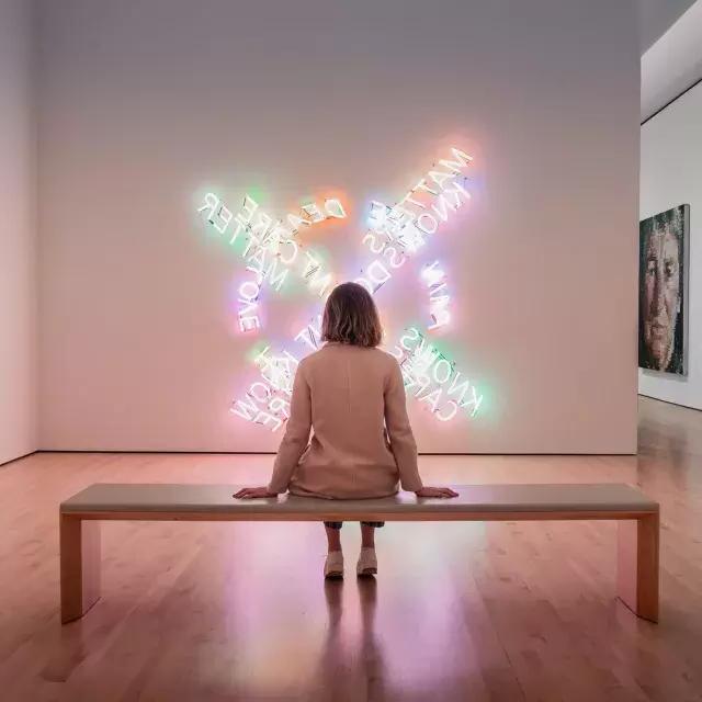 샌프란시스코 SF MOMA에서 벤치에 앉아 현대 조명 예술 작품을 감상하는 여성.