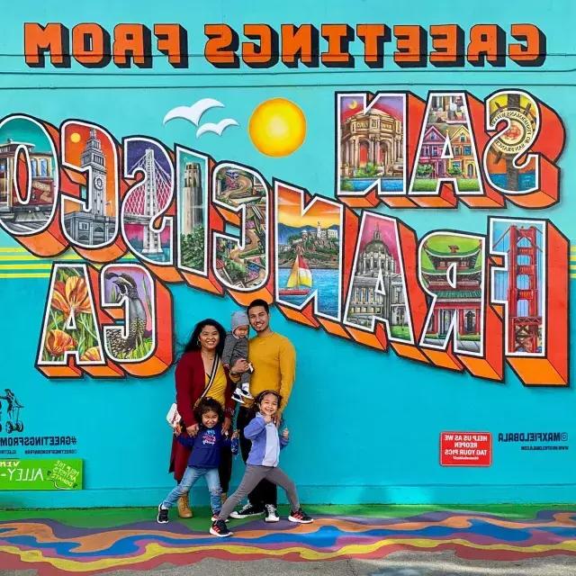 Uma família posando para uma foto em frente a um mural de São Francisco