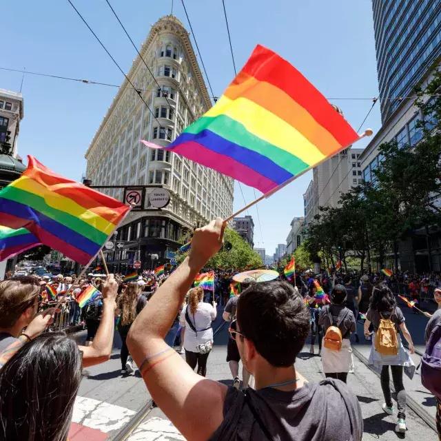 Pessoas andando na Parada do Orgulho de São Francisco agitam bandeiras de arco-íris.