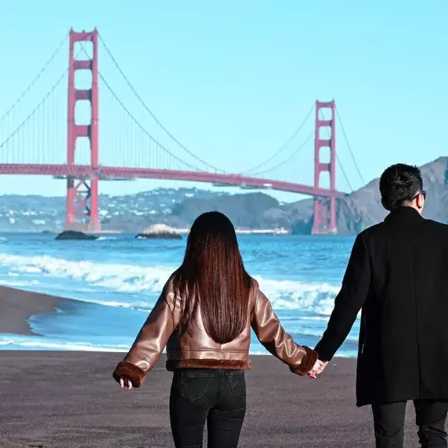 Pareja tomados de la mano en Baker Beach con el puente Golden Gate en segundo plano 